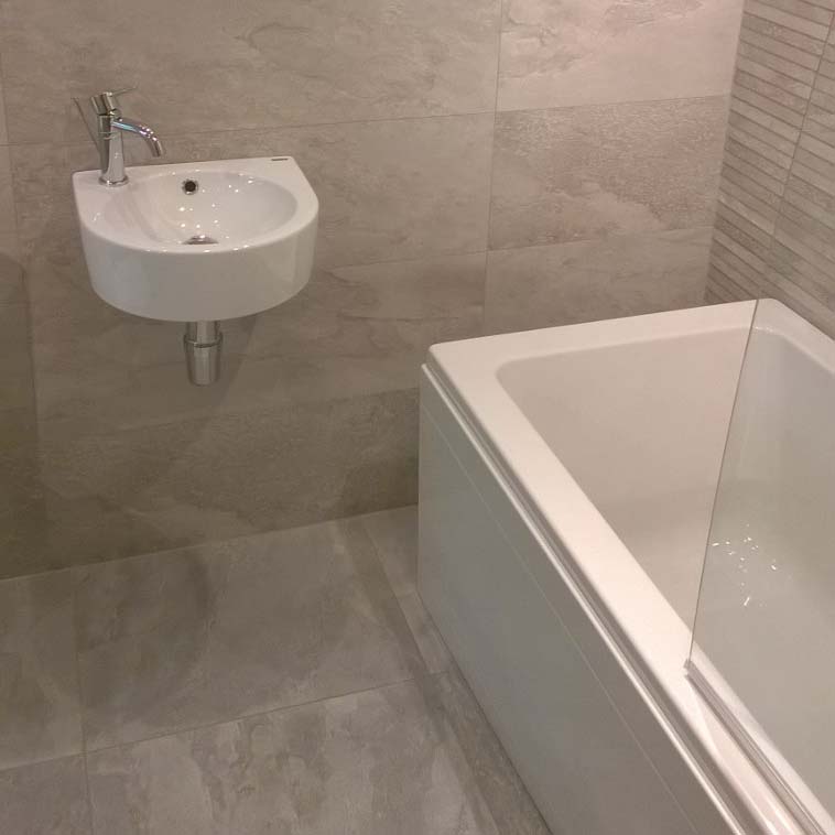 Grey tiled bathroom with bath and small sink